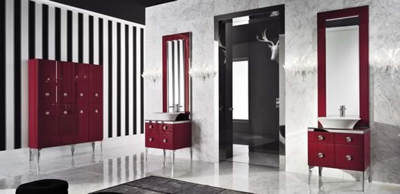 Cuarto de baño con paredes a rayas blancas y negras, lavabo en color blanco sobre modular rojo con cajones. Pared independiente de mármol blanco y bordes de mármol negro.
